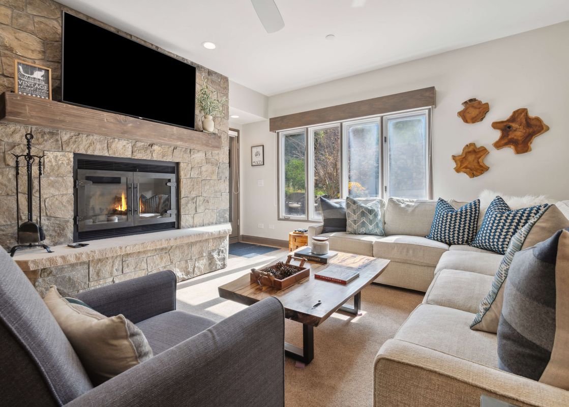A cozy living room with a large stone fireplace, television, sectional sofa, and wooden coffee table at The Charter F2305.