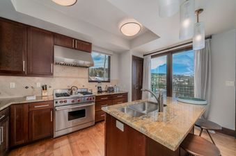 The modern kitchen of Lumiere 2 Bedroom Suite features stainless steel appliances, a large island with bar stools, and large windows with mountain views.