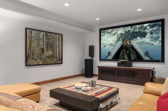 A home theater room with a large projector screen, leather sofas, and a coffee table.