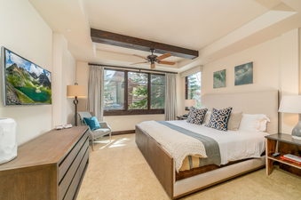 The master bedroom at Lumiere Three Bedroom Luxury features a plush king bed, a large flat screen TV, and a seating area with a comfortable chair.