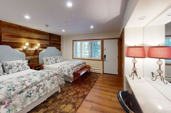 The bedroom at Manor Vail 148A has two queen beds, floral bedding, a wood-paneled wall, and a vanity with a mirror.