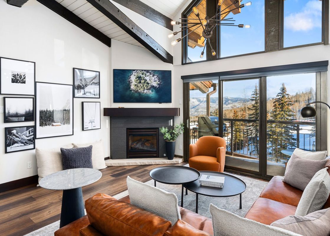 A spacious living room with a brown leather sectional sofa, a fireplace, and large windows offering a snowy mountain view.