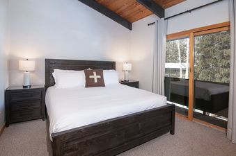 A bedroom with a king-sized bed, two nightstands with lamps, and a large window with a view of the trees outside.