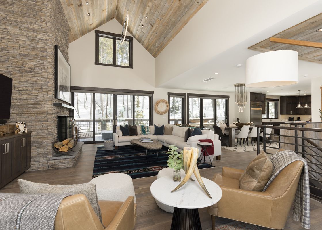 The grand living room at Spanish Peaks Highlands Cabin 36, featuring a stone fireplace, vaulted wooden ceilings, a large sectional sofa, and expansive windows overlooking a snowy landscape.