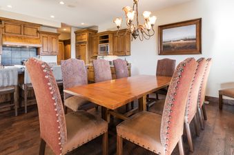 A sophisticated dining room at Silver Star 39 featuring a large wooden table surrounded by elegant, studded upholstered chairs, with a view of the adjacent kitchen.