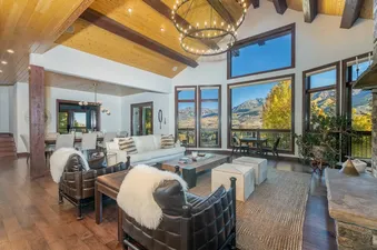 The spacious great room at Evergreen with vaulted ceilings, leather armchairs, a white sofa, and massive windows offering breathtaking mountain views.