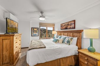 The primary bedroom at Bear Claw 2 Valley View 513 features a queen-sized bed, a wooden dresser with a TV, a window with a view, and a ceiling fan.