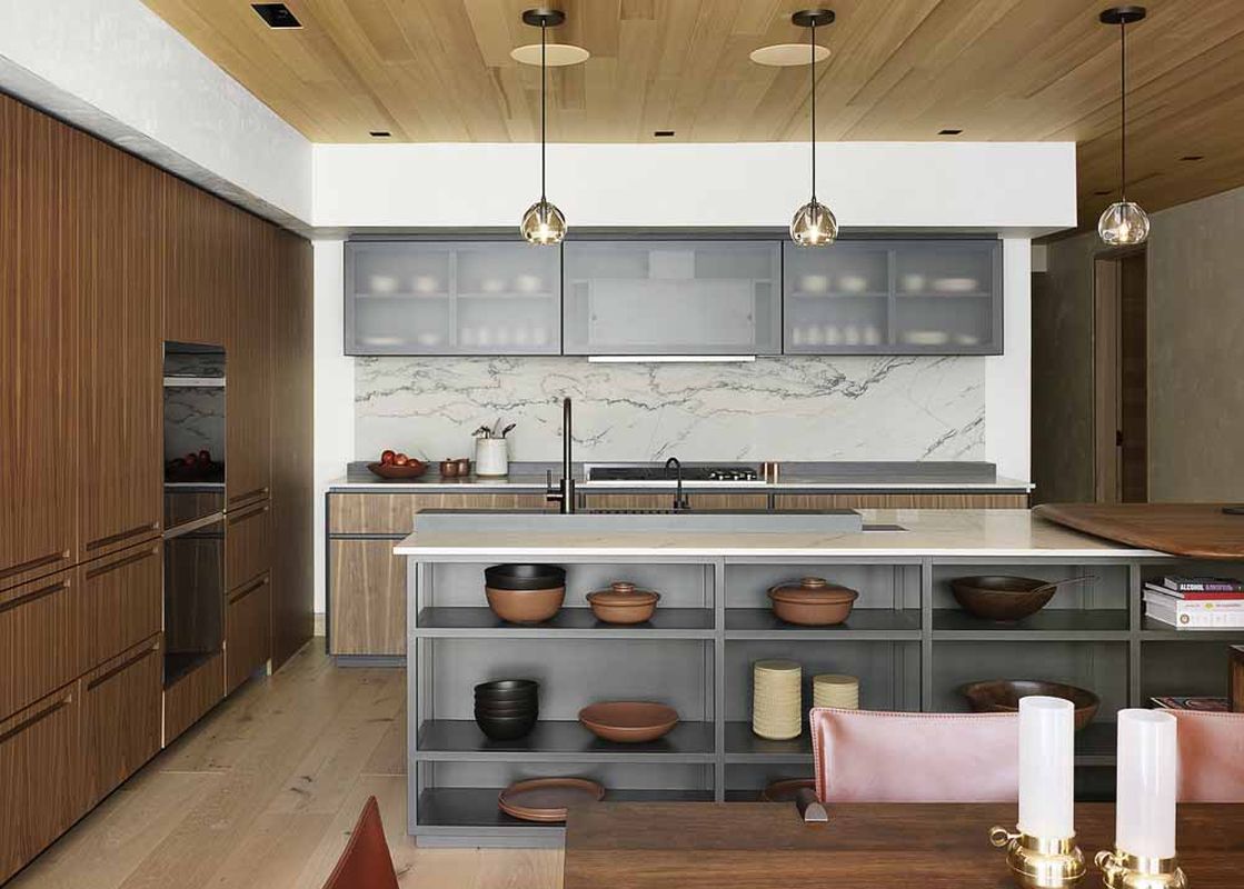 A modern kitchen with wooden cabinetry, a large kitchen island, and contemporary pendant lights, creating an inviting and luxurious atmosphere.