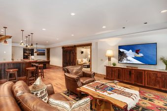 Spacious family room at Forest Edge with leather seating, a large TV, and an integrated wet bar.