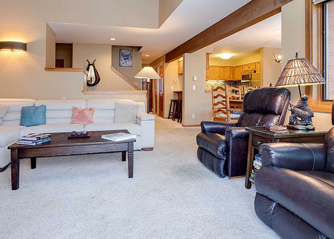 An expansive multi-level living area inside the Ranch at Steamboat RA606, showcasing a white sectional, a dark leather sofa area, modern lighting, and a glimpse of the kitchen.