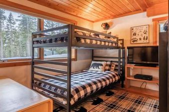 A bunk bed with a checkered comforter in a cabin style bedroom.