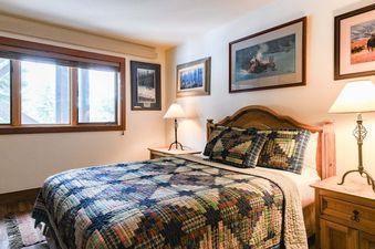 A rustic bedroom in Nez Perce A6 featuring a wood frame bed with a patchwork quilt and framed art on the wall.