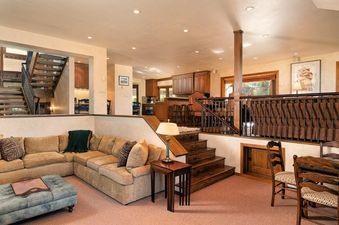 The open-concept living area at Woodrun V Residence 5 features a sectional sofa, an ottoman, and a wooden staircase, all contributing to a warm and inviting atmosphere.