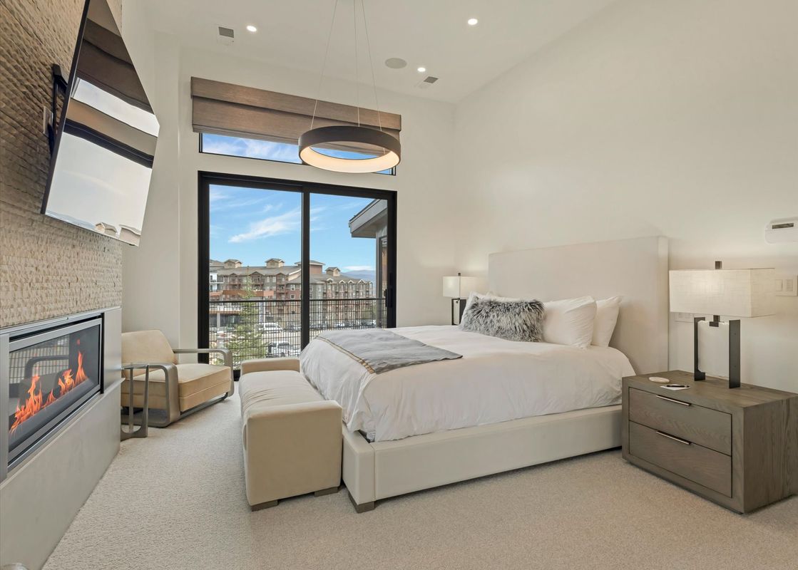 Modern and elegant bedroom at Sunrise Ridge at Canyons with a king bed, fireplace, and sliding door to a balcony.