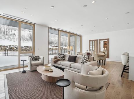 The open-concept living area at Founders Place 2304 features a light gray sofa and armchairs, an oval coffee table, and large windows with snow-covered views.
