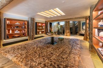 A cozy and rustic great room featuring a large, shaggy area rug, wooden display shelves with decorative items, and natural tree trunks serving as structural elements.