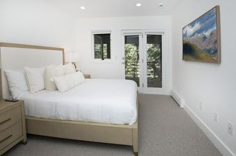 The comfortable king bedroom features a large bed with white linens, nightstands, a wall-mounted TV, and access to a private balcony with outdoor views in Rockledge 325.