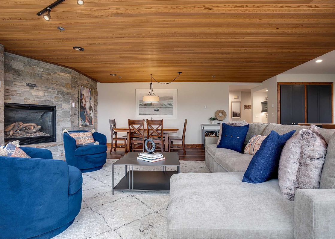 The living area of Chateau Chamonix CX211 features a cozy sectional sofa, two blue armchairs, a stylish coffee table, and a grand stone fireplace.