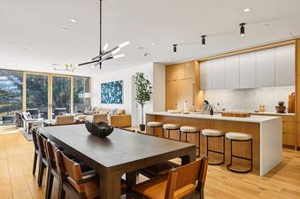 A spacious, modern open-concept kitchen and dining area in Founders Place 2502 with a large wooden dining table and chairs, a kitchen island with bar stools, and large windows looking out to a snowy mountain and forest.