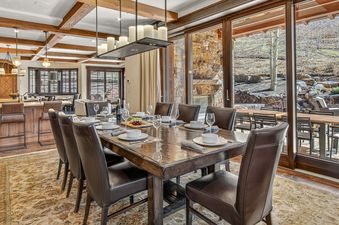 A dining table set for a meal with brown leather chairs and an elegant chandelier in High Road's dining area.