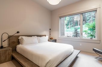Moonlight Basin 80B Lodgeside bedroom featuring a king-size bed with crisp white linens and a large window with a view of the forested landscape.