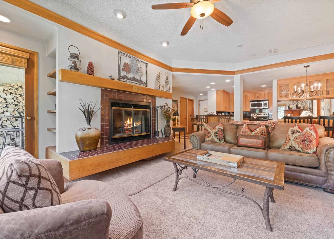 A cozy living room in The Charter A3505 with a lit fireplace, a large brown sofa, and an armchair, connecting to an open-plan kitchen and dining area.