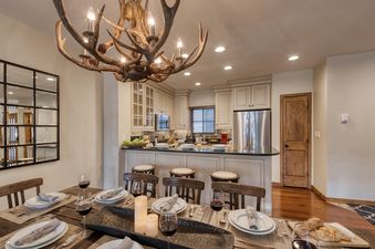 The dining area and kitchen of Chalet Fortessa, featuring a rustic antler chandelier and a fully set wooden dining table.