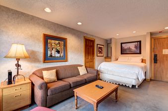 A hotel room with a queen bed, a sofa, and a small coffee table.