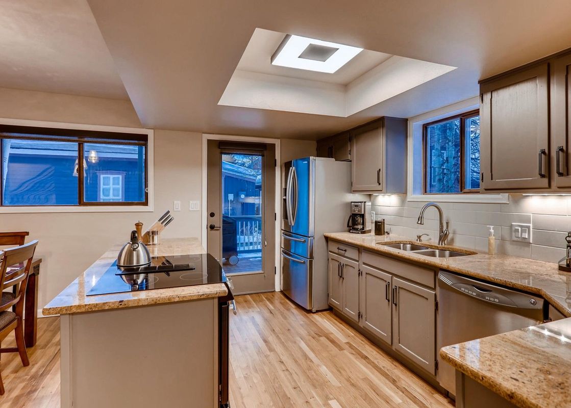 The kitchen at High Street Retreat features light wood floors, grey cabinets, and granite countertops.