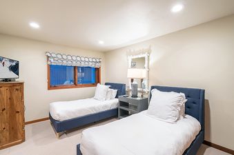 Two twin beds with white linens and navy blue headboards are located in a bedroom with wood floors, a large window, and a dresser.