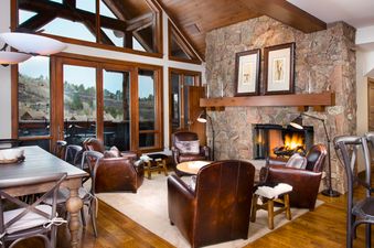 The grand living area of the Bear Paw Lodge 4 Bedroom Plus Loft boasts a magnificent stone fireplace and large windows offering stunning mountain views.
