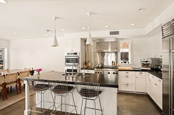 A modern kitchen with white cabinets, stainless steel appliances, a large island with bar stools, and an adjacent dining area.