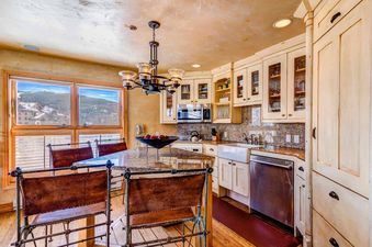 The kitchen at Peaks Penthouse 752 features a large island with seating, a white farmhouse sink, and views of snowy mountains through the window.