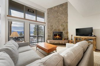 A spacious living room at Meadow Ridge 31 features comfortable seating, a stone fireplace, and large windows offering scenic mountain views.