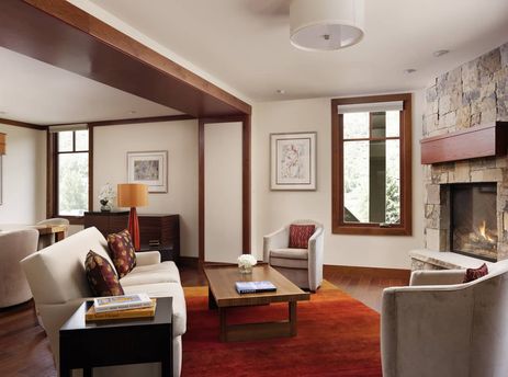 Living room with sofa, rich wooden floors, red area rug, fireplace, two grey armchairs