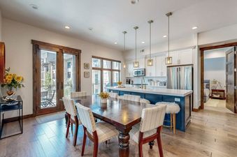 A modern open-concept dining area and kitchen in the Modern Blackstone Paradise 2A, featuring a wooden dining table, blue kitchen island, and stainless steel appliances.
