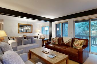 A spacious and inviting living area in Teewinot C3 with a brown leather sofa, armchairs, and sliding doors leading to a balcony.