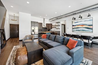 A modern open-concept living space with a gray sectional sofa, a dark wood coffee table, and an integrated kitchen and dining area.