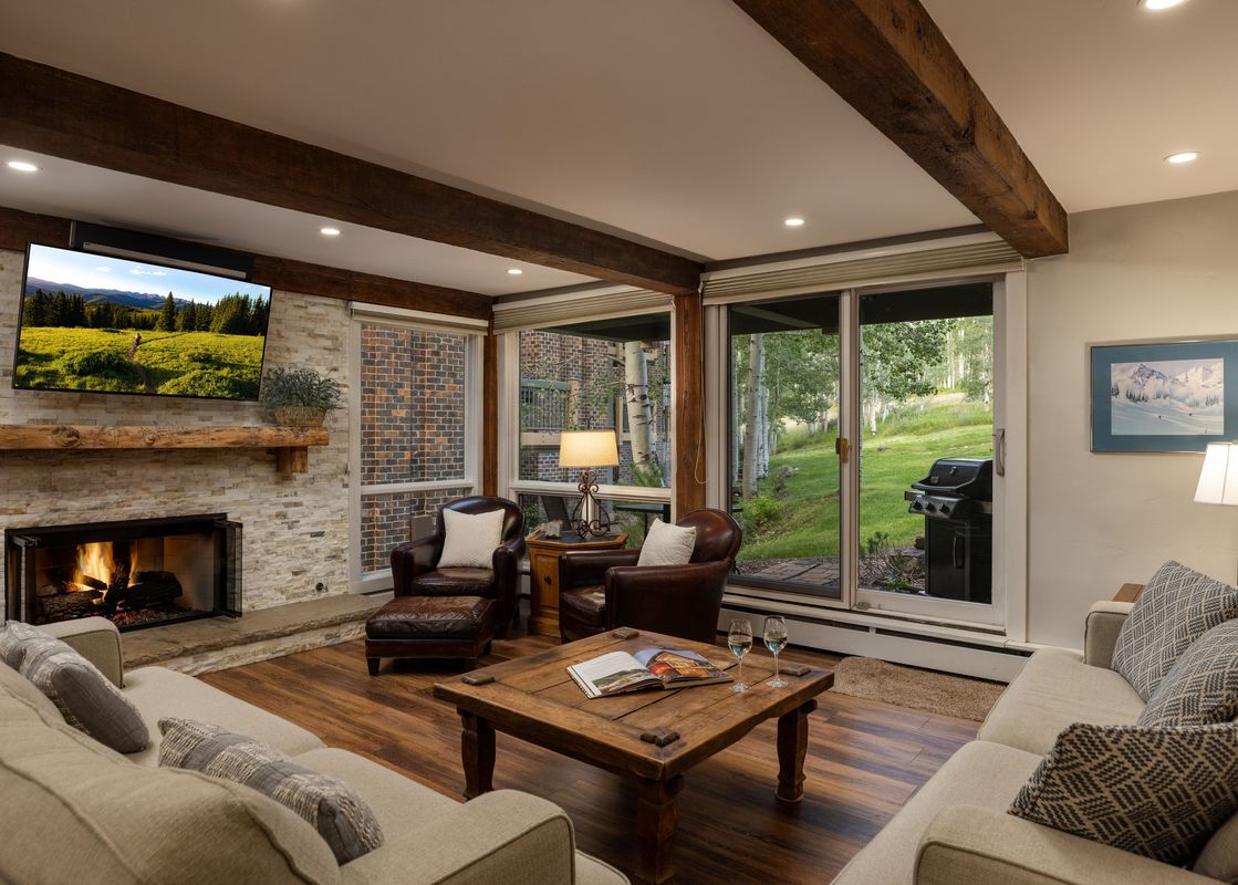 Cozy living room in Top of the Village Trails 101 with a stone-surfaced fireplace, leather armchairs, beige sofas, and a view of the green lawn outside.