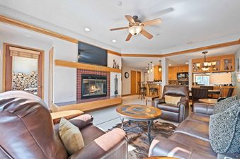 A cozy living room in The Charter D3705 with a fireplace, comfortable leather sofas, and an open layout leading to the kitchen and dining area.