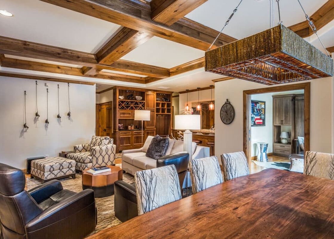 The Chateau Beaver Creek Residence 1304's open-concept living and dining areas feature exposed wooden beams, a large dining table, comfortable seating, and a built-in bar.