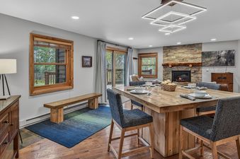 Dining table and chairs set in First Tracks Chalet with a stone fireplace in the background.