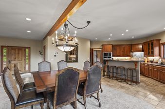 The dining area at Grand View on the Blue features a wooden table, upholstered chairs, and an elegant chandelier, with a full kitchen visible in the background.