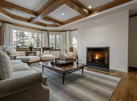 A luxurious living room in Chateau Beaver Creek Residence 1403 with a roaring fireplace, large windows showcasing a snowy view, comfortable seating, and exposed wooden ceiling beams.