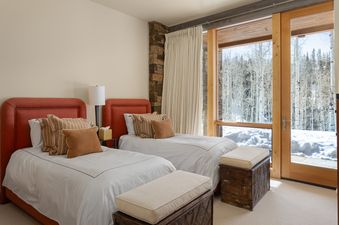 A cozy twin bedroom at Skyline Estate featuring two twin beds, orange headboards, and a large window looking out onto a snow-covered forest.