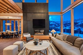 The Havens Summit's luxurious living room with a modern fireplace, comfortable sofa, and floor-to-ceiling windows offering a panoramic view of snow-covered mountains.