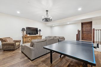 A spacious entertainment room at Slopeside 117 with a comfortable seating area, television, and a ping-pong table on hardwood floors.