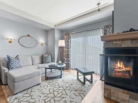 The St Regis Family Valley View Suite living room features a fireplace and a plush sectional sofa, with a large window and patterned curtains.