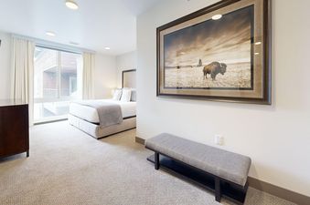 The master bedroom at Peak Retreat with a large bed, TV console, bench, and artwork of a bison.
