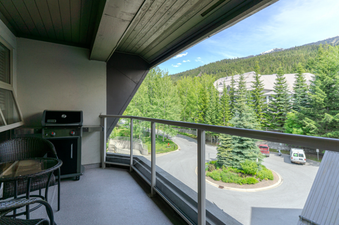 A private balcony at the Aspens on Blackcomb Unit 438, featuring a BBQ grill and a dining set, with a view of a lush green landscape and mountains.